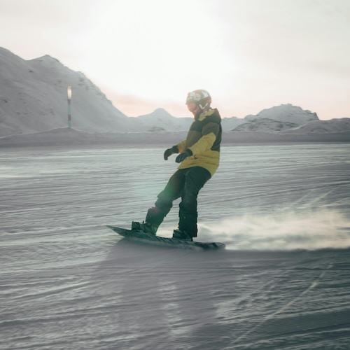 snowboarder doing a power slide in the sunset